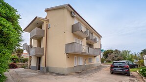 Un palazzo residenziale a più piani con balconi, un'auto parcheggiata davanti e cielo sereno.