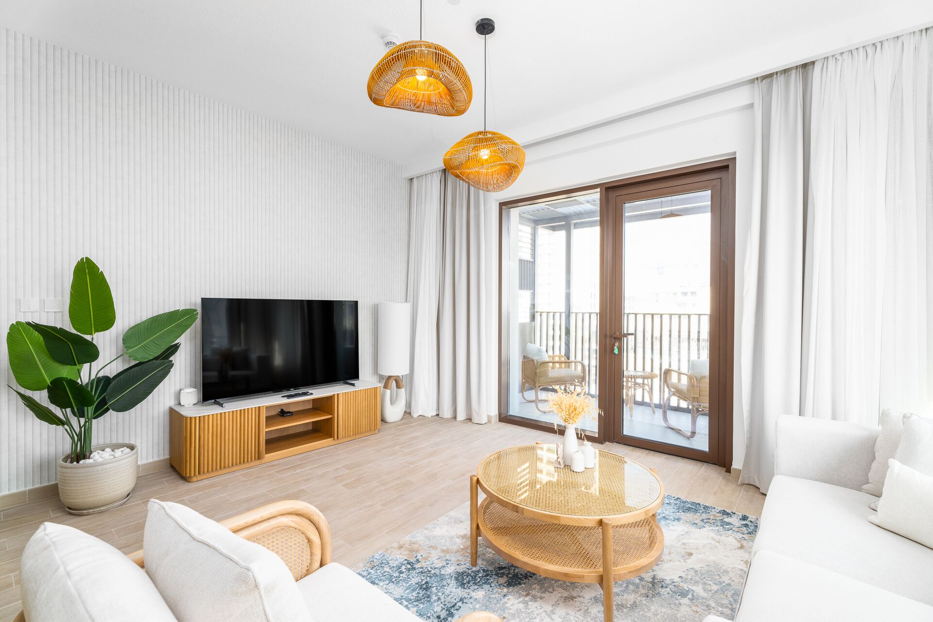Ein modernes Wohnzimmer mit Fernseher, Rattanmöbeln und einem Balkon mit Korbmöbeln.