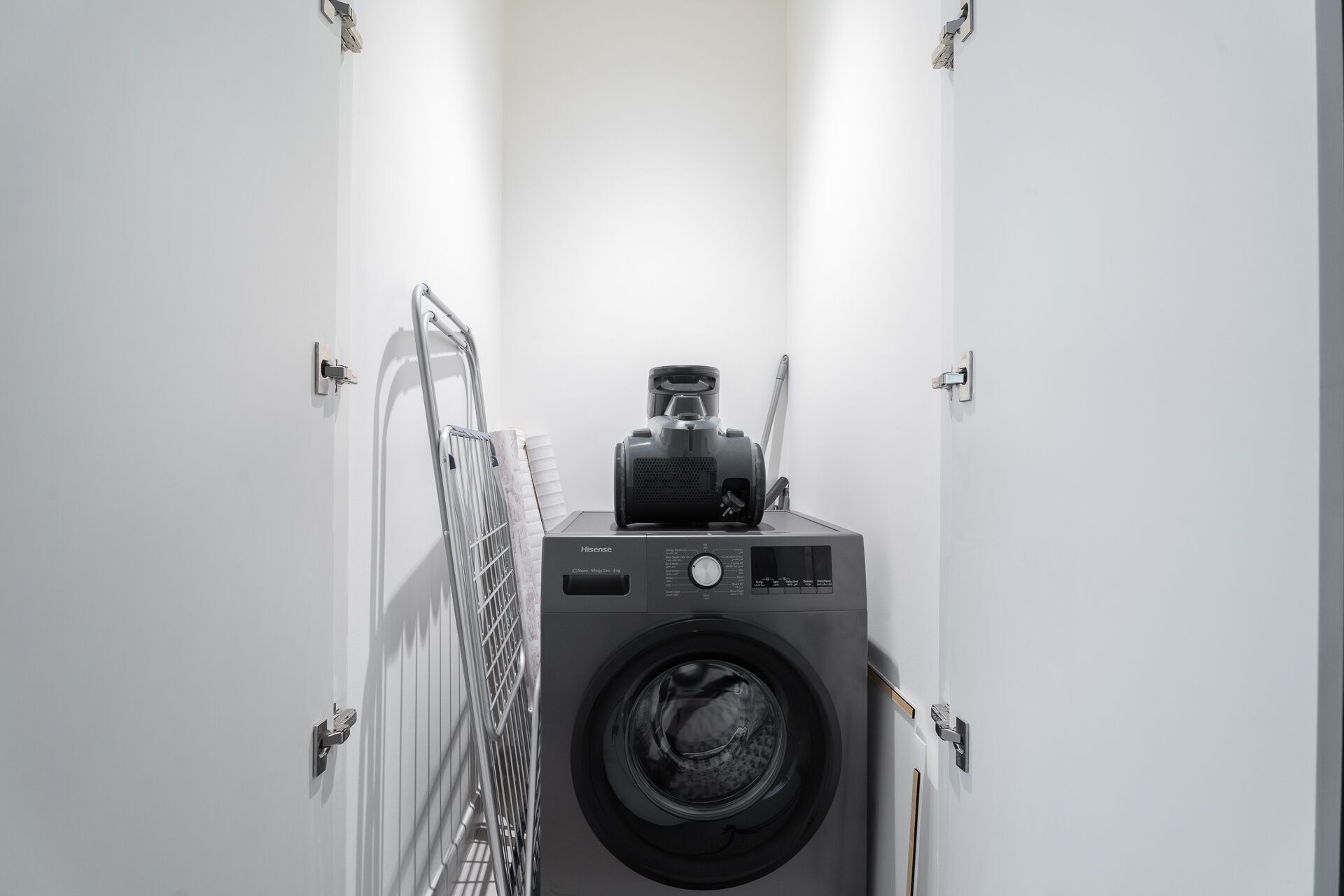 A compact, modern laundry room with a front-loading washing machine and a drying rack.