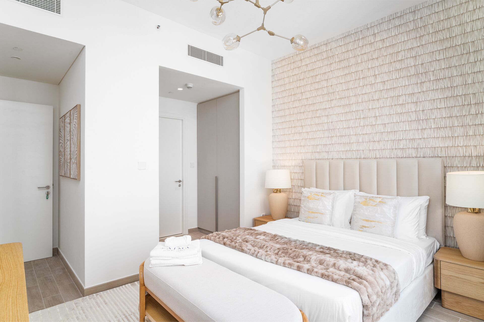A modern bedroom with a large bed, two bedside tables, a hanging light fixture, and a textured wall.