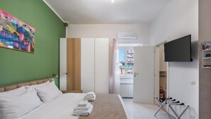 Ein Hotelzimmer mit Bett, Fernseher, Wäscheständer und einer grünen Wand mit einem farbenfrohen Gemälde.