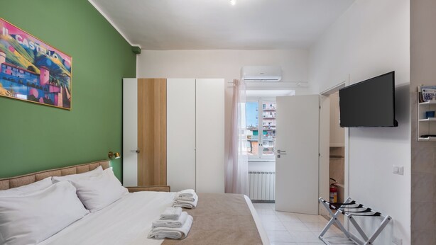 Ein Hotelzimmer mit Bett, Fernseher, Wäscheständer und einer grünen Wand mit einem farbenfrohen Gemälde.