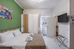 Habitación de hotel con cama, televisor, tendedero y pared verde con un cuadro de colores.