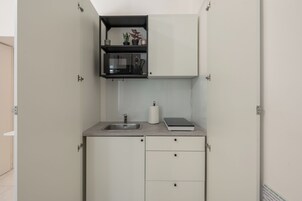 Una cocina compacta con microondas integrado, un lavamanos y una pequeña encimera.