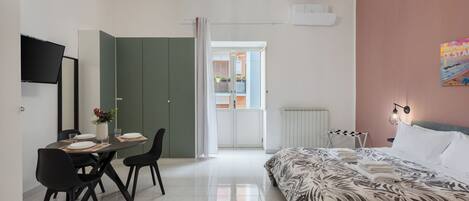 Ein modernes Schlafzimmer mit einem Bett, einem Schreibtisch mit Stühlen, einem Esstisch und einem Fernseher.