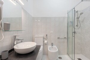 Un baño moderno con un lavamanos ovalado grande, un bidé y una zona de ducha con mampara de vidrio.