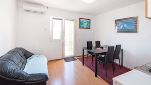A room with a sofa, a dining table with chairs, a small kitchen area, and a door with a window. - Ivica two Bedroom Apartment L, Novalja (Novalja)