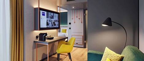 A modern hotel room with a desk, a yellow chair, a green sofa, and a TV mounted on the wall.
