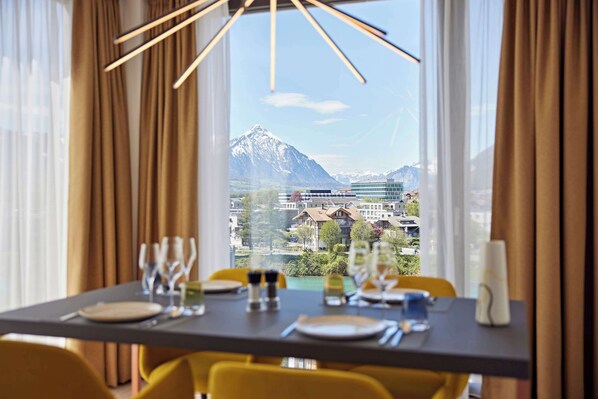 A dining table set for four with a mountain view through large windows. - Essential by Dorint Interlaken (Interlaken)