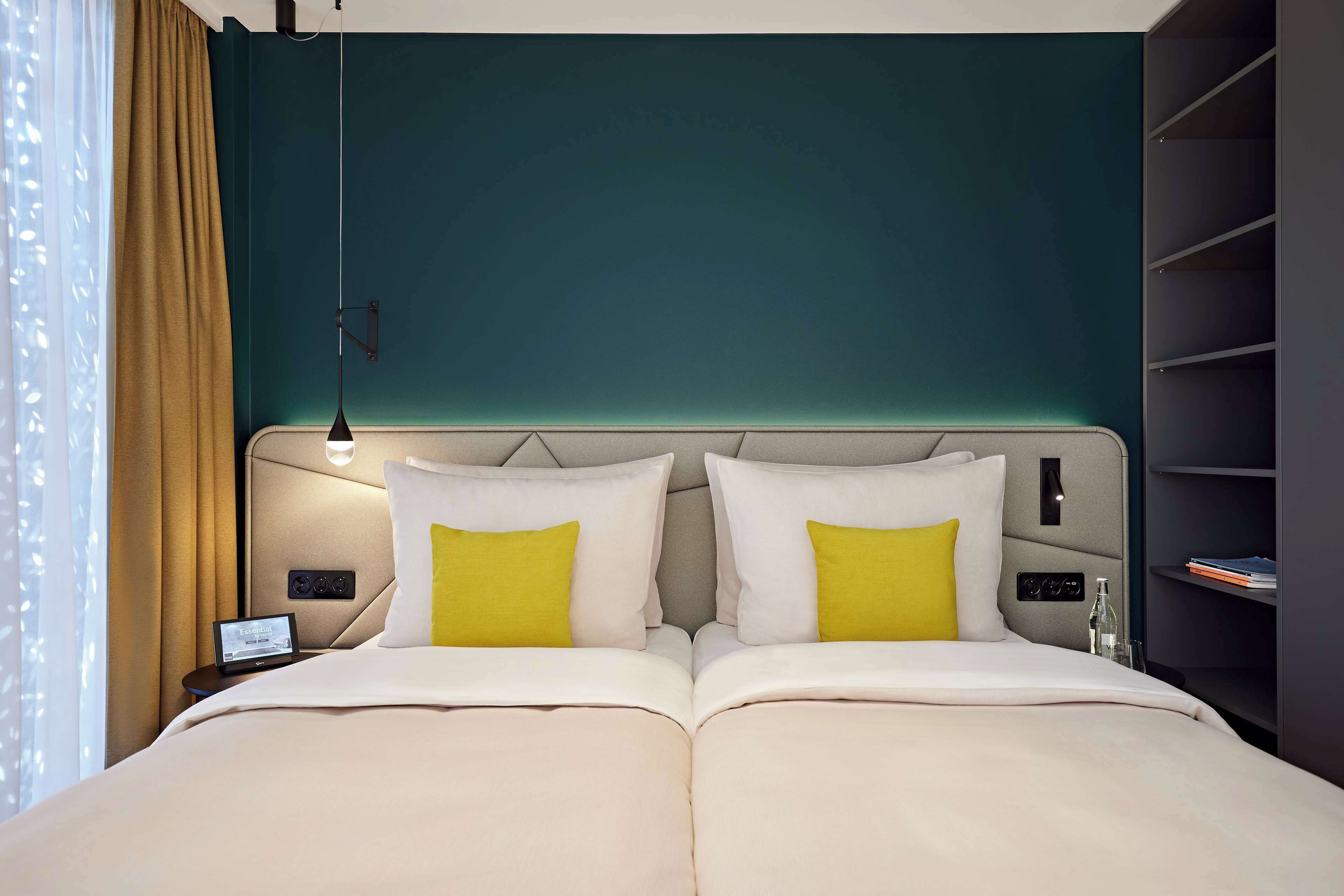 A modern hotel room with a large bed, two bedside tables, a nightstand, and a built-in shelving unit.
