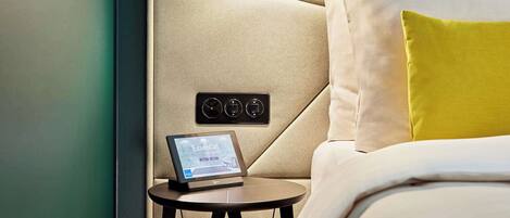 A neatly made bed with a headboard, a bedside table with a tablet, and a pendant light.