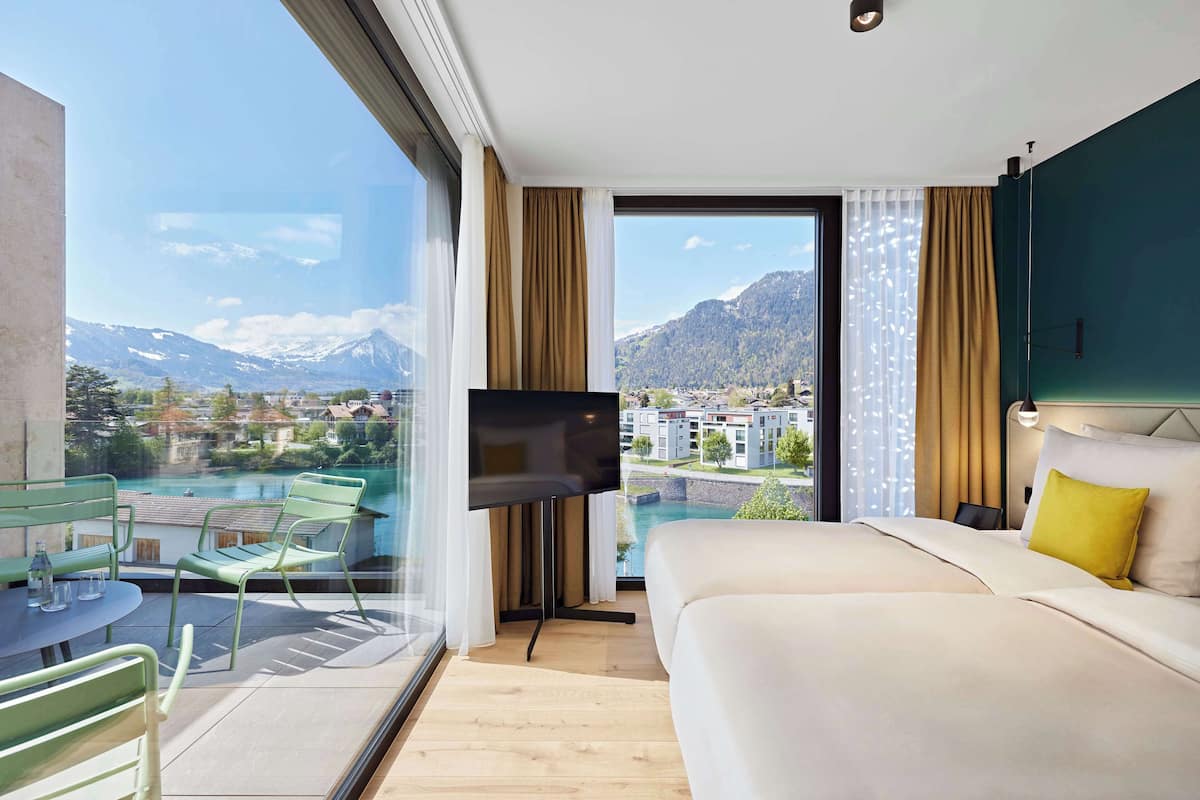 A hotel room with a large bed, a TV, a balcony with a view of mountains and a lake.