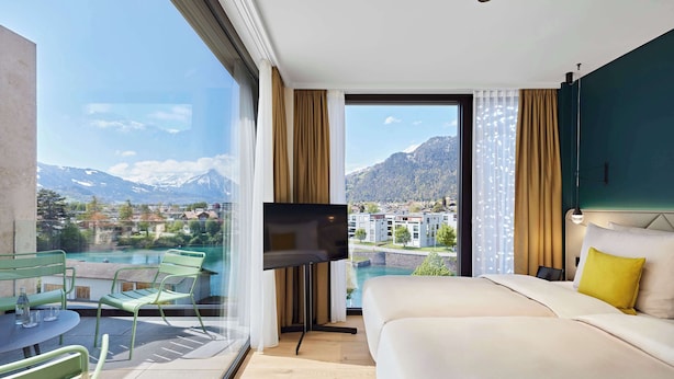 Ein Hotelzimmer mit einem großen Bett, einem Fernseher, einem Balkon mit Blick auf Berge und einen See.