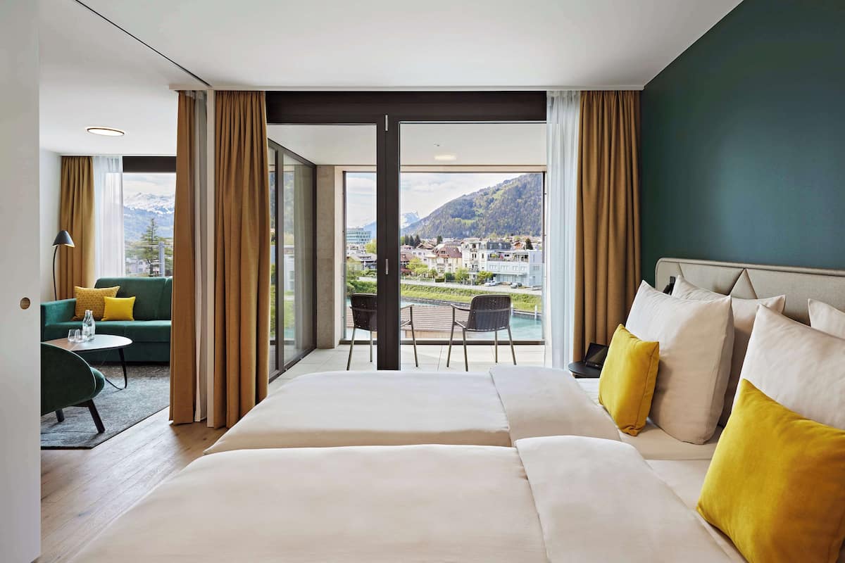 A hotel room with a large bed, a sofa, and a balcony with a view of a town and mountains.