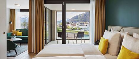 Une chambre d’hôtel avec un grand lit, un canapé et un balcon offrant une vue sur la ville et les montagnes.