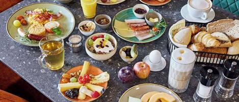A breakfast buffet with various dishes, drinks, and condiments on a marble table.