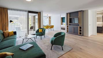 Quarto de hotel moderno com sofá verde, cadeiras amarelas, mesa de jantar e aparador para TV.