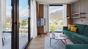 Ein modernes Hotelzimmer mit Balkon, einem grünen Sofa, einem Couchtisch und einem Flachbildfernseher.