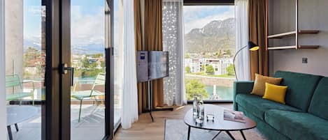 Una habitación de hotel moderna con balcón, un sofá verde, una mesa de centro y un televisor de pantalla plana.