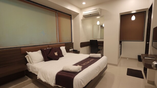 A modern hotel room with a large bed, a desk, a chair, an air conditioning unit, and a mirror.