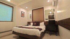 A hotel room with a bed, a desk, an air conditioner, a mirror, and a window.