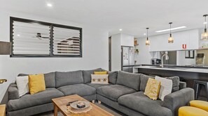 A modern living room with a grey sectional sofa, a wooden coffee table, and a kitchen area with white cabinets and pendant lighting. - Yarrawonga Lakeside apartment 43 -  3 Bedrooms (Mulwala)