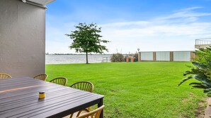 A patio with a table and chairs, a grassy lawn, a tree, and a view of a body of water.
