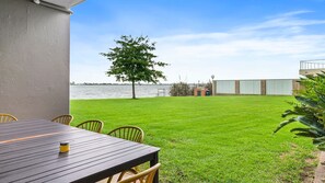A patio with a table and chairs, a grassy lawn, a tree, and a view of a body of water.