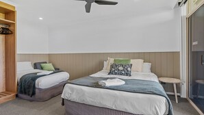 A hotel room with two beds, a ceiling fan, a small round table, and a wardrobe.