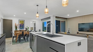 Une cuisine moderne dotée d’un îlot central, d’un coin repas avec une table et des chaises, d’un four encastré et de luminaires suspendus.