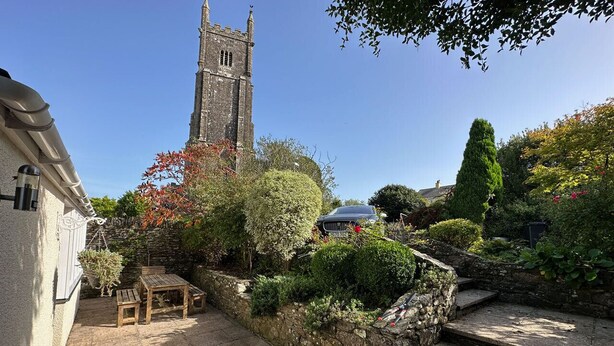 A stone staircase leading up to a building with a tower, surrounded by lush greenery and a wooden table and chairs. - The Glen, Ugborough, South Devon (Ugborough)