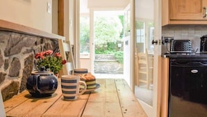A kitchen with a stone wall, wooden table, and a view of the garden. - The Glen, Ugborough, South Devon (Ugborough)