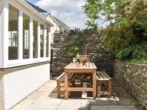 A wooden bench and table set against a stone wall, with a window and greenery visible.
