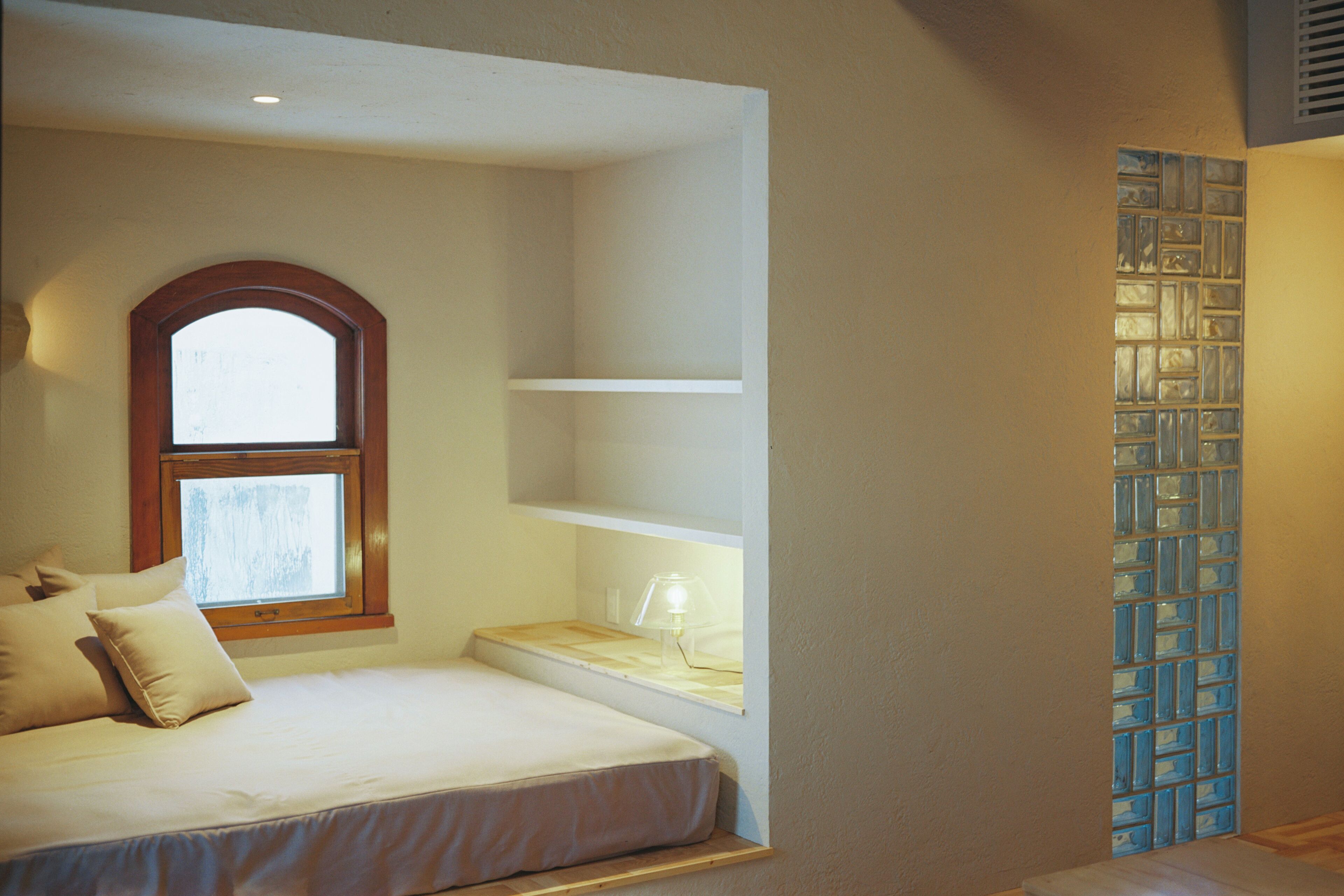 A bedroom with a bed, a window, a shelf, and a wall with a patterned design.
