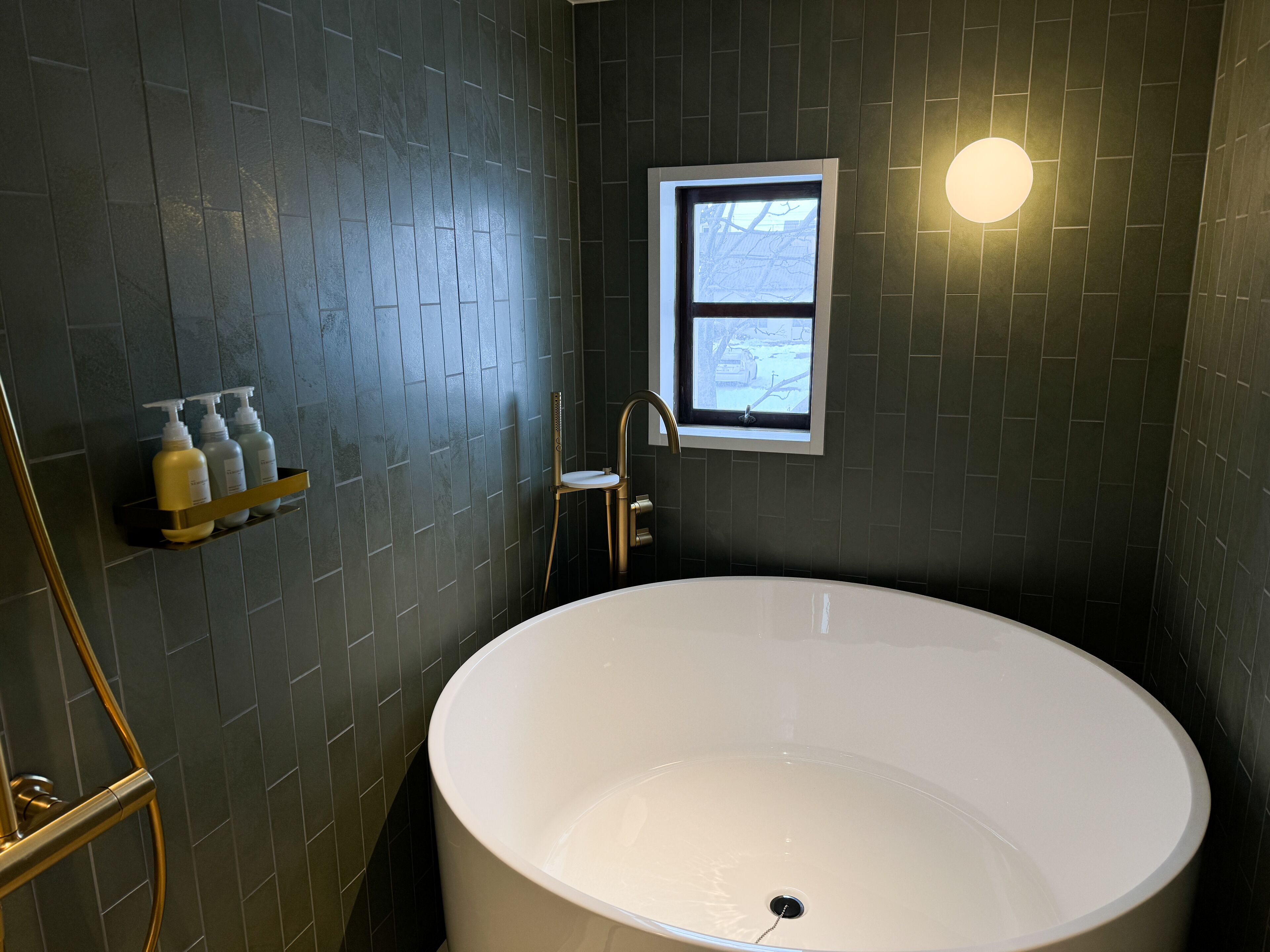 Un baño moderno con una bañera independiente, un ventanal y un estante con artículos de aseo.