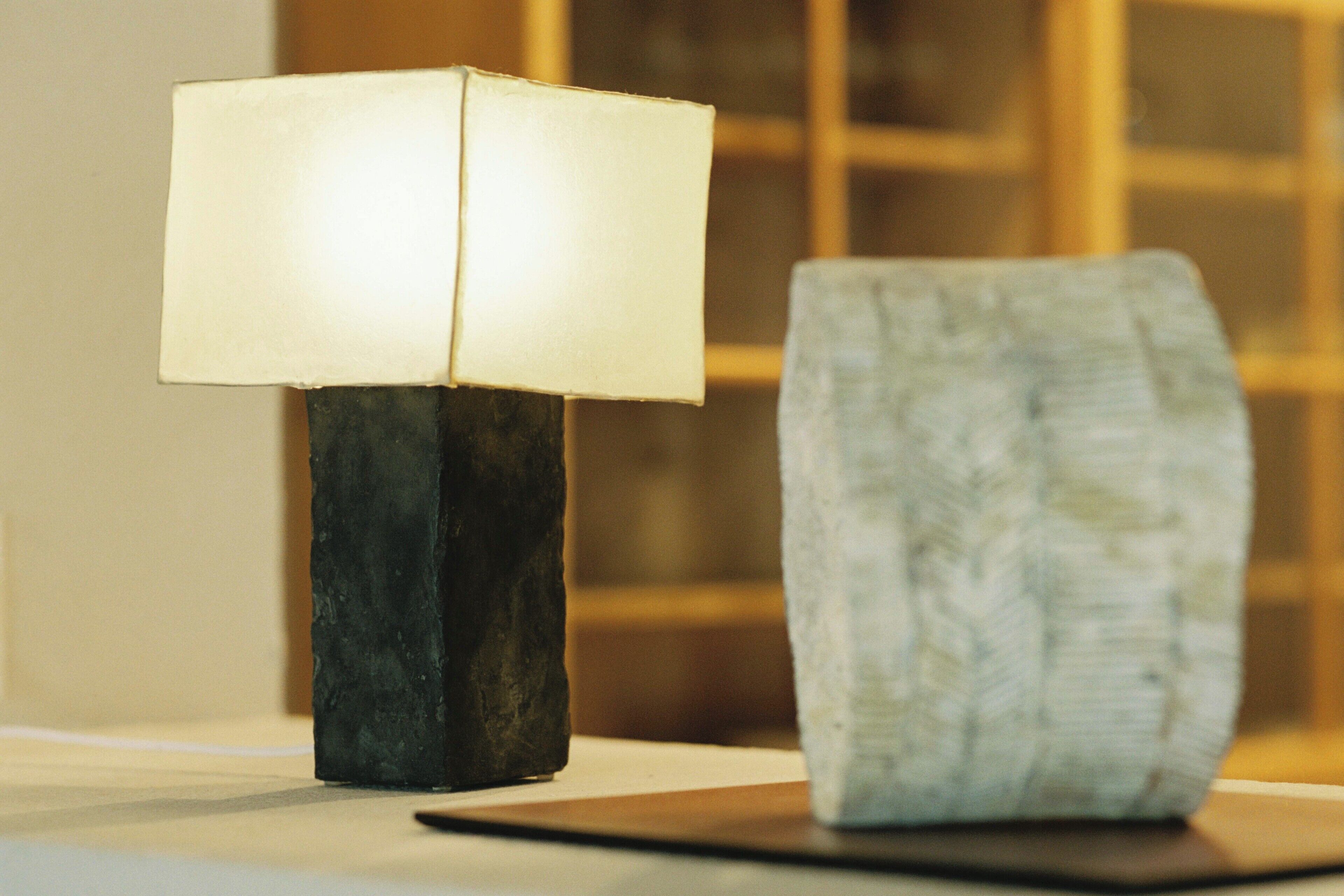 A modern table lamp with a square shade on a dark base, placed on a white surface.
