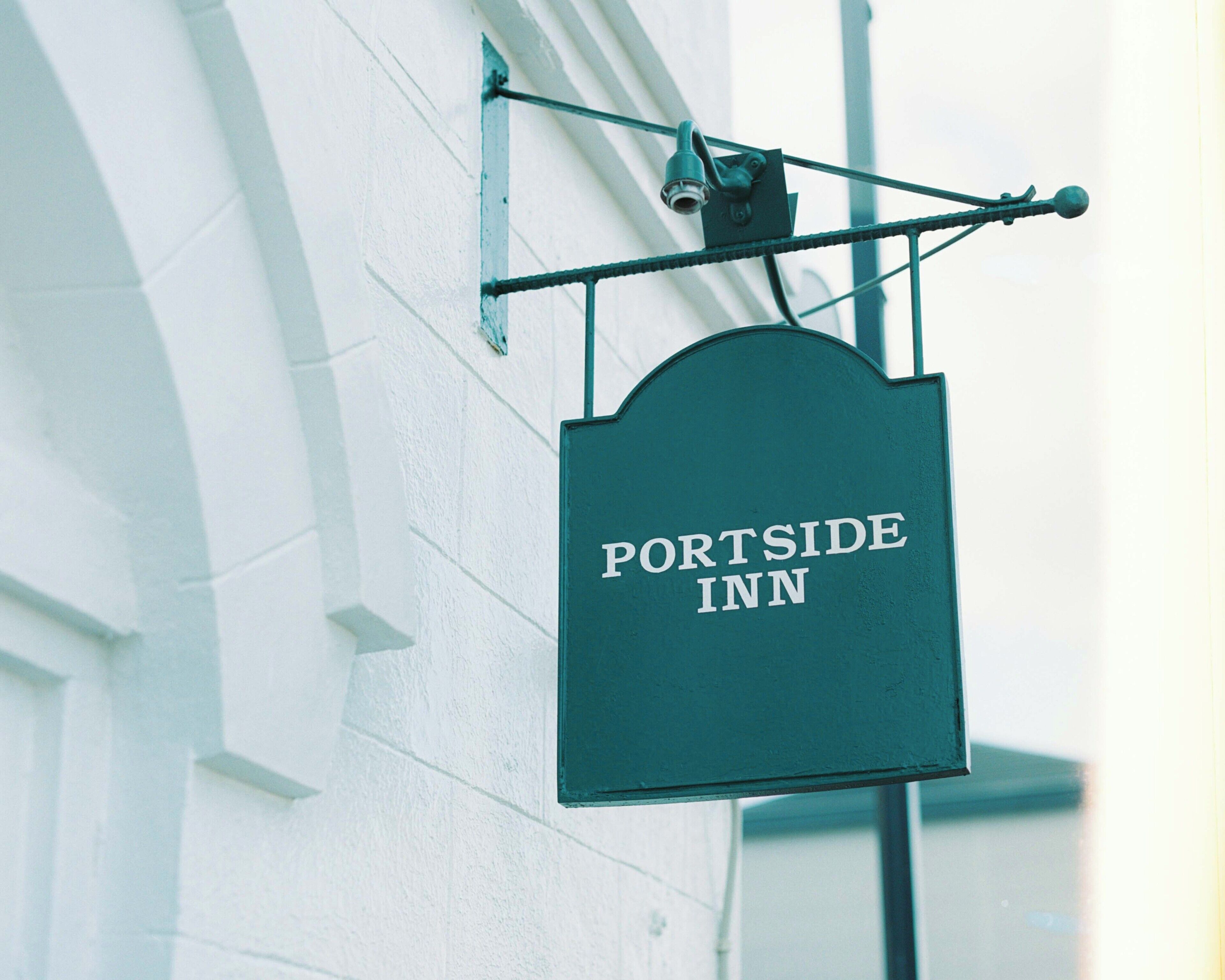 A sign for the Portside Inn, mounted on a metal bracket against a white building facade.