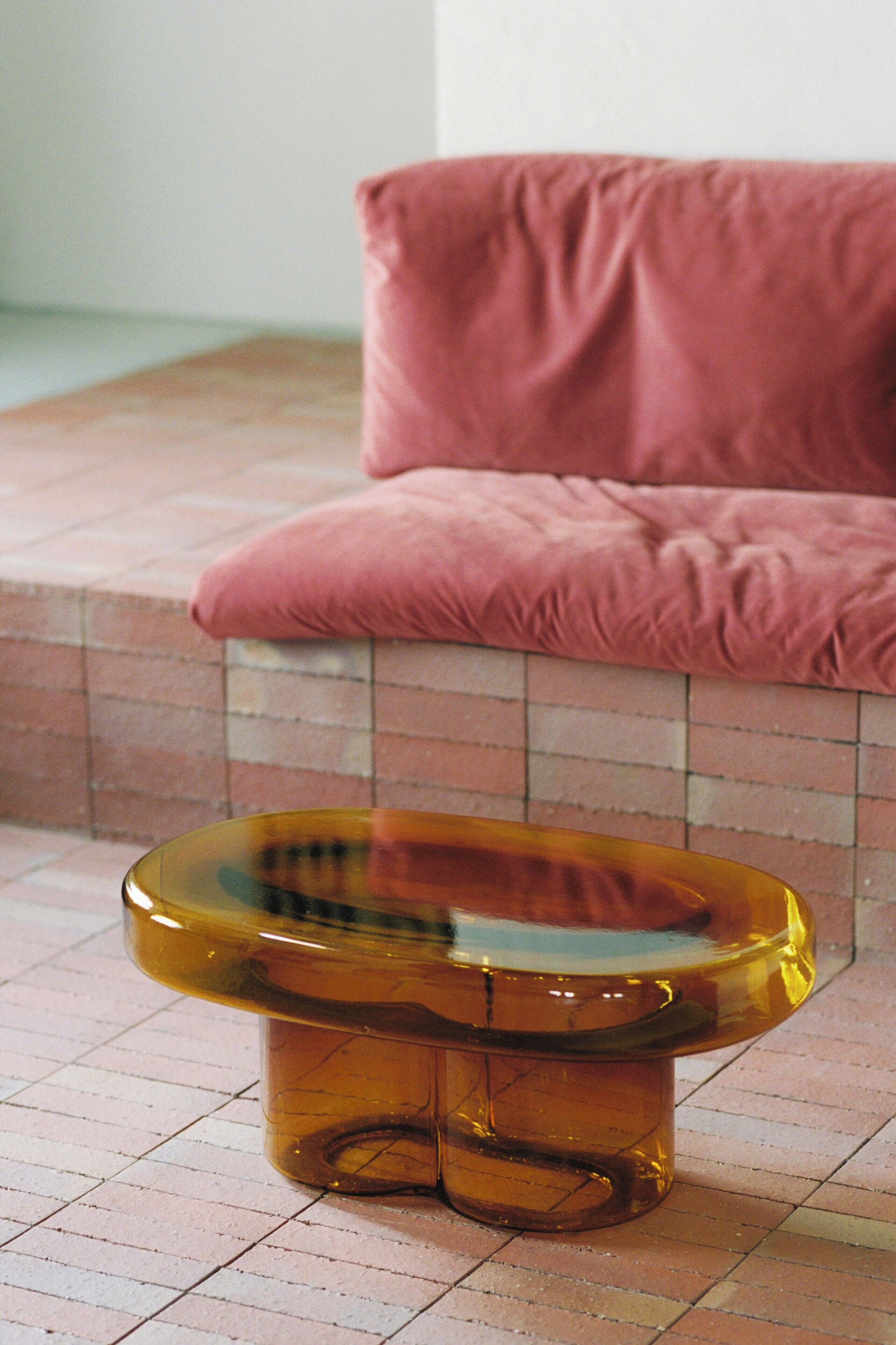 Una mesa de cristal transparente con superficie reflectante, ubicada sobre un suelo de baldosas.
