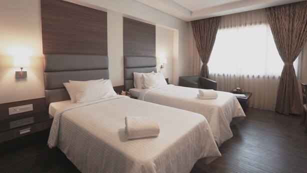 A hotel room with two beds, a desk, a chair, and a window with curtains. - Fressotel Seetharam (Coimbatore)