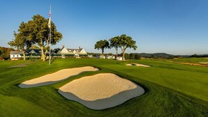 En golfbane med bunkers, et flag og en klubhus i baggrunden.