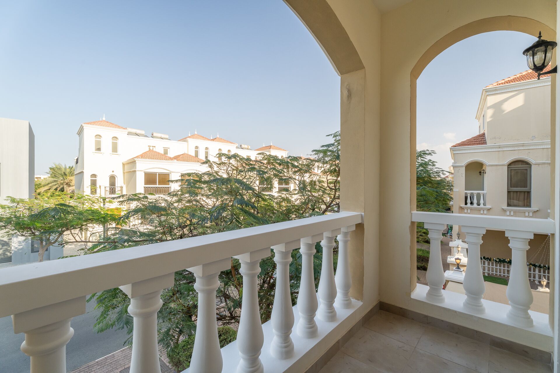 A balcony with white balustrades overlooking a residential area with white buildings and greenery.
