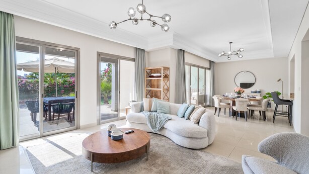Un salon spacieux avec un grand canapé, une table basse et un coin repas comprenant une table ronde et des chaises. Une porte-fenêtre coulissante donne accès à un patio extérieur équipé d’une table et de chaises.