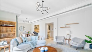 Un salon spacieux avec un grand canapé d’angle, une table basse ronde et un lustre moderne.