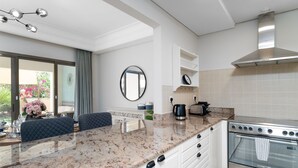 Une cuisine moderne dotée de plans de travail en granit, de meubles blancs, d’une hotte en acier inoxydable et d’un four encastré.