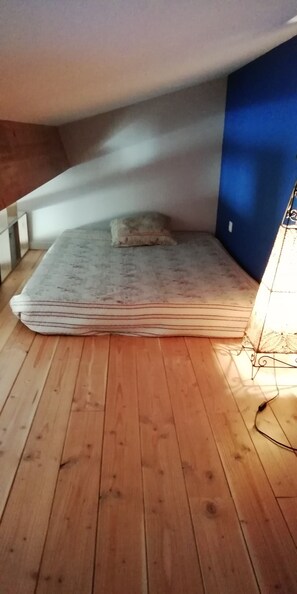 Un pequeño y tenuemente iluminado ático con una cama individual y techo inclinado.