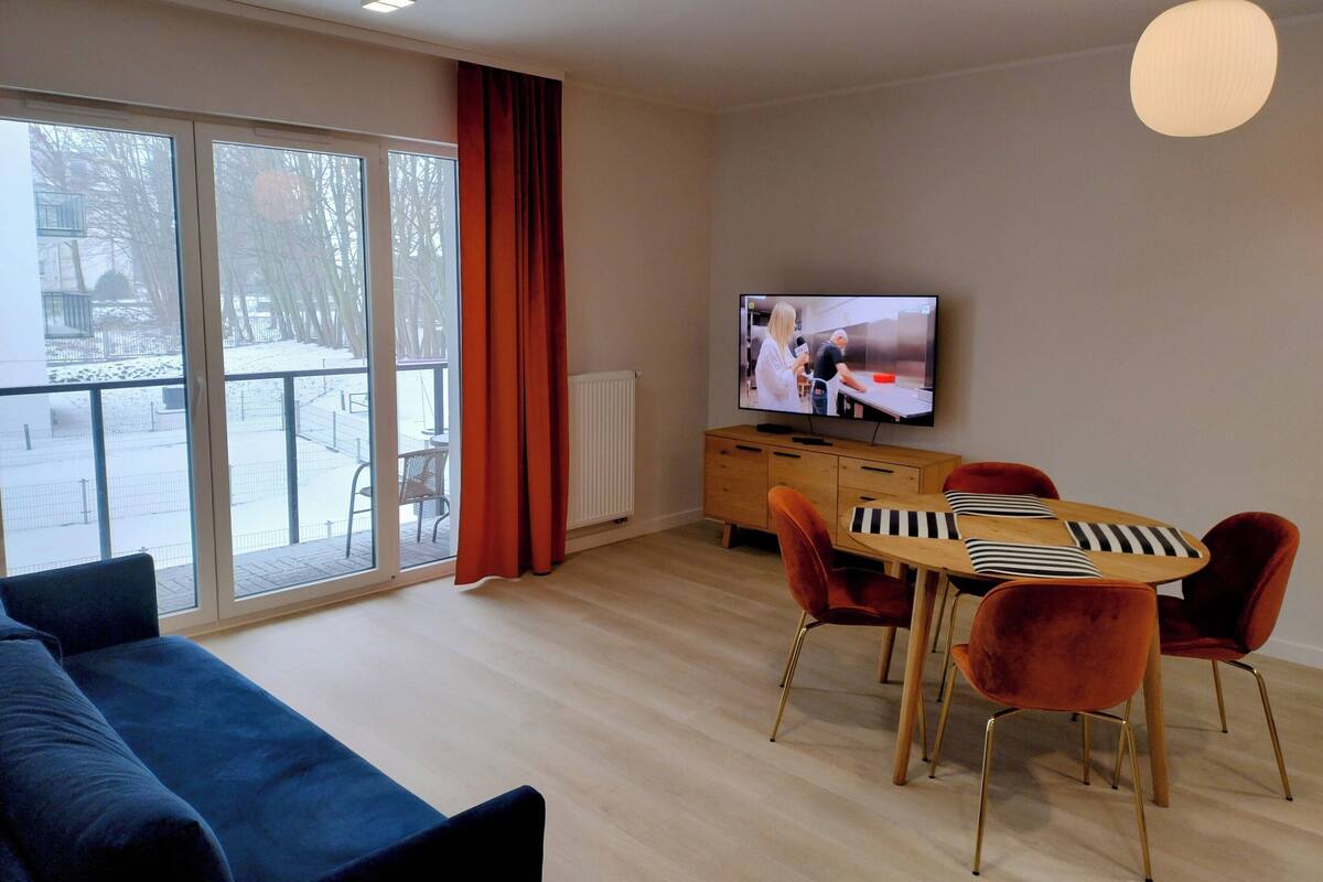 Una sala de estar moderna con un televisor grande, una mesa de comedor con cojines a rayas y un sofá.