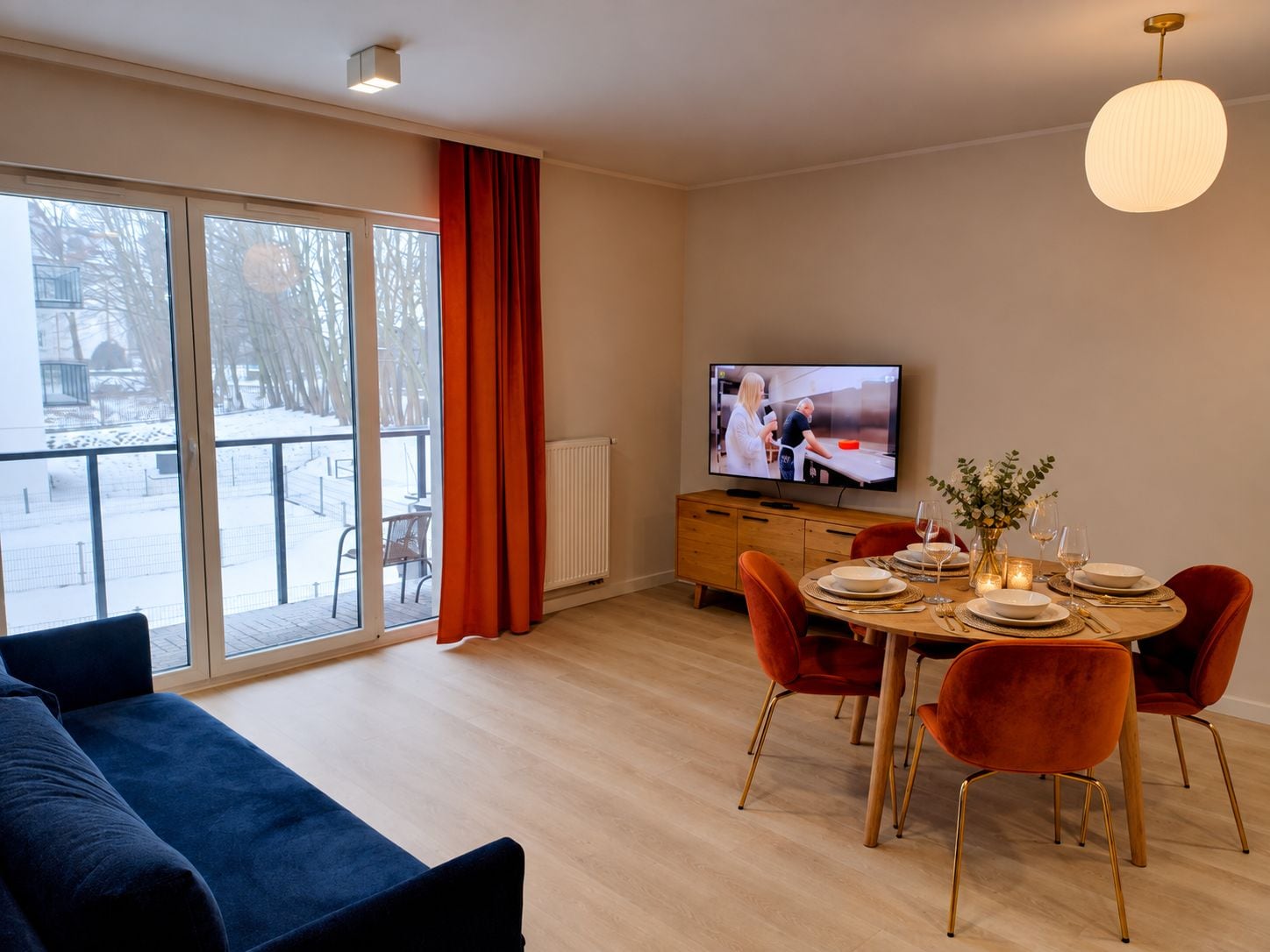 A modern living room with a sofa, dining table set for four, and a television.