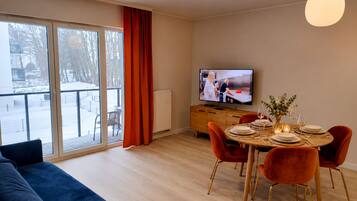 A modern living room with a sofa, dining table set for four, and a television.