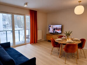 A modern living room with a sofa, dining table set for four, and a television.