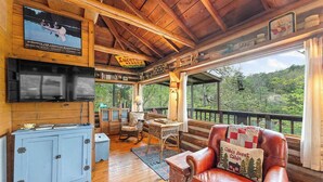 Een cabin interieur met een houten plafond, een aan de muur bevestigde televisie, een blauwe kast, een leren bank en uitzicht op de natuur.